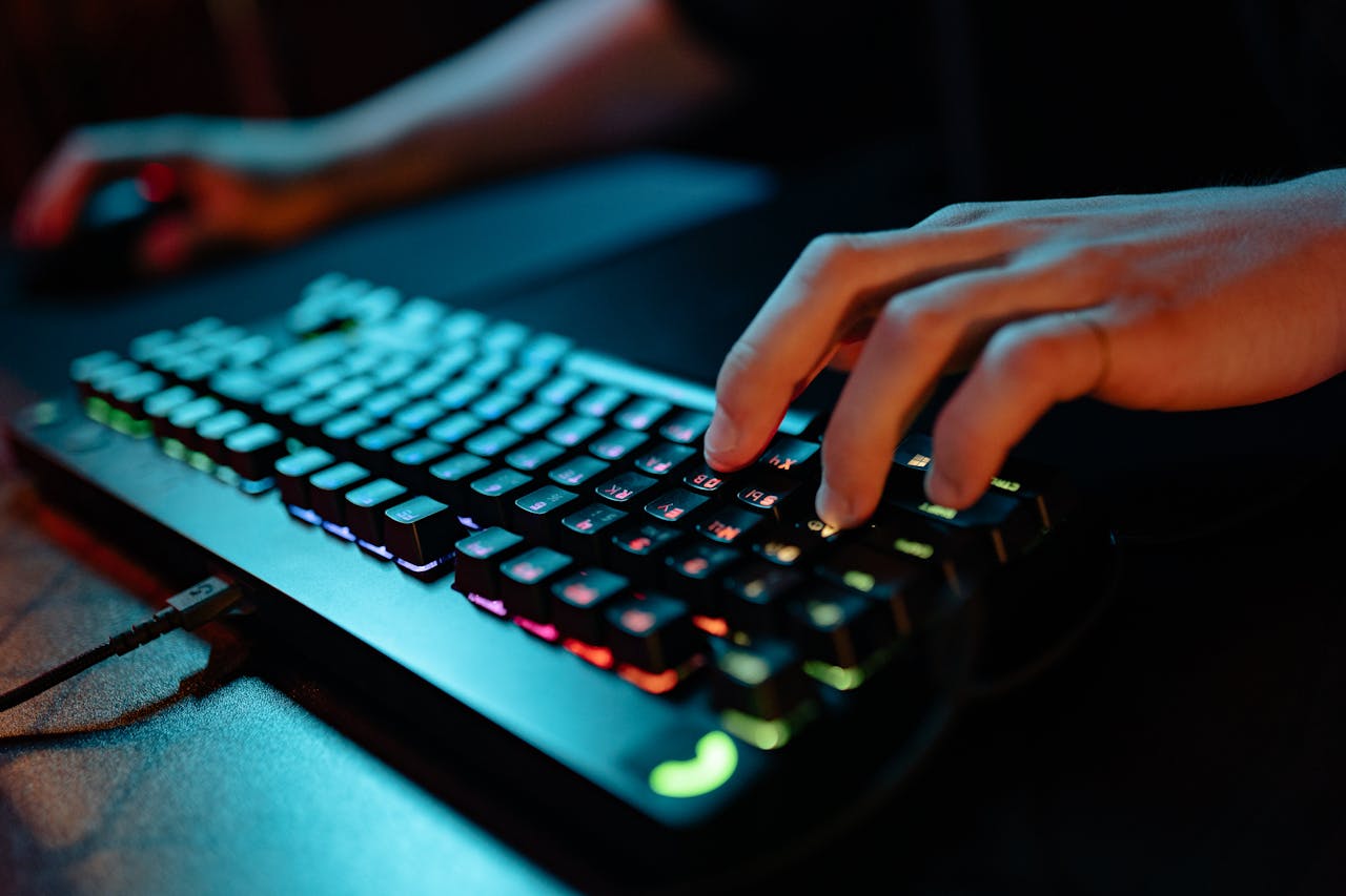 Hands typing on a glowing RGB keyboard during a gaming session indoors.